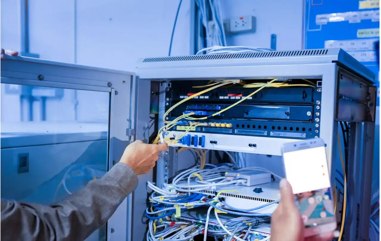 Technician organizing Ethernet and fiber cables inside a network rack, illustrating structured cabling systems and color-based cable identification in commercial network environments