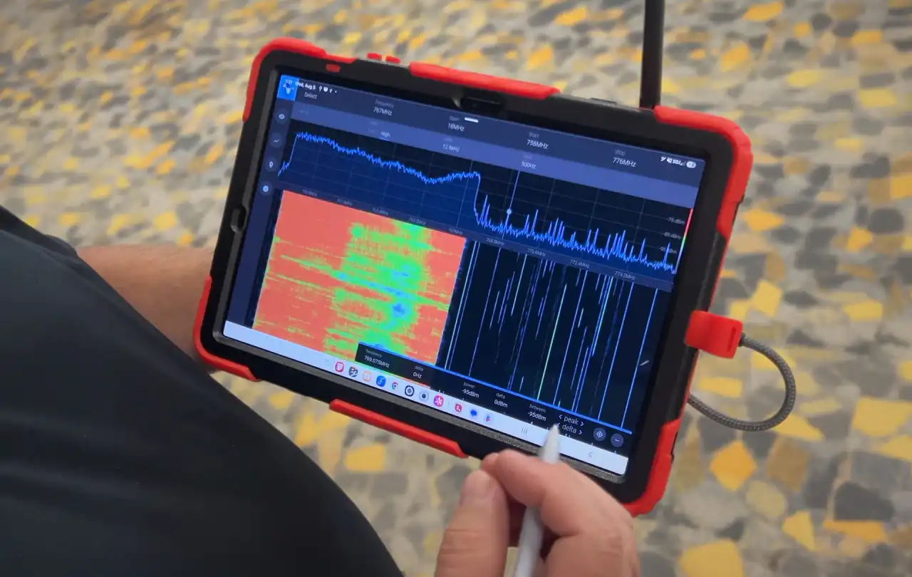 Windy City Wire technician using a tablet-based RF spectrum analyzer to perform ERCES public safety in‑building grid testing, with spectrum and waterfall graphs visible