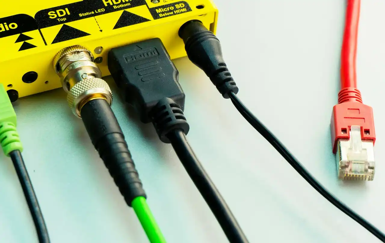 Close-up of a yellow electronic device with SDI, HDMI, power, and Ethernet cables connected, shown on a light-colored surface.