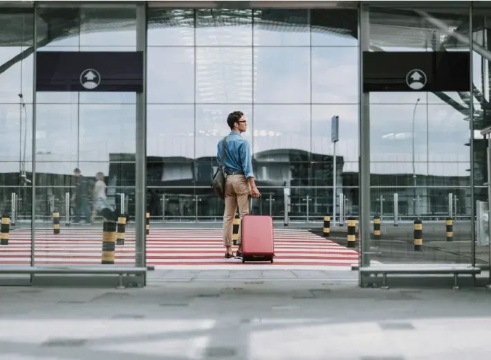 Traveler with a suitcase waiting outside automatic sliding entrance doors at an airport terminal, the type of low-voltage controlled door hardware wired with access control cable