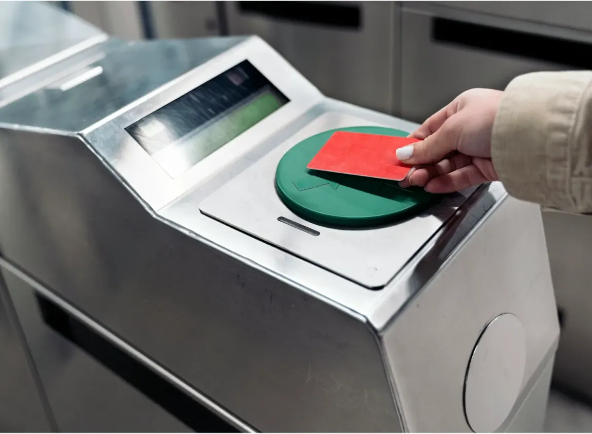 Hand tapping an access card on a green contactless card reader mounted on a security turnstile, the type of access control hardware wired with 18 AWG 6-conductor security cable