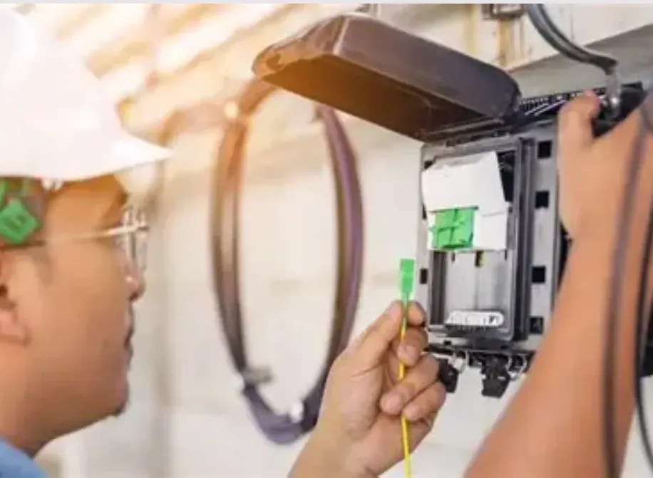 Close-up of a fiber optic install—installer connects a yellow patch cord with a green connector to a distribution enclosure
