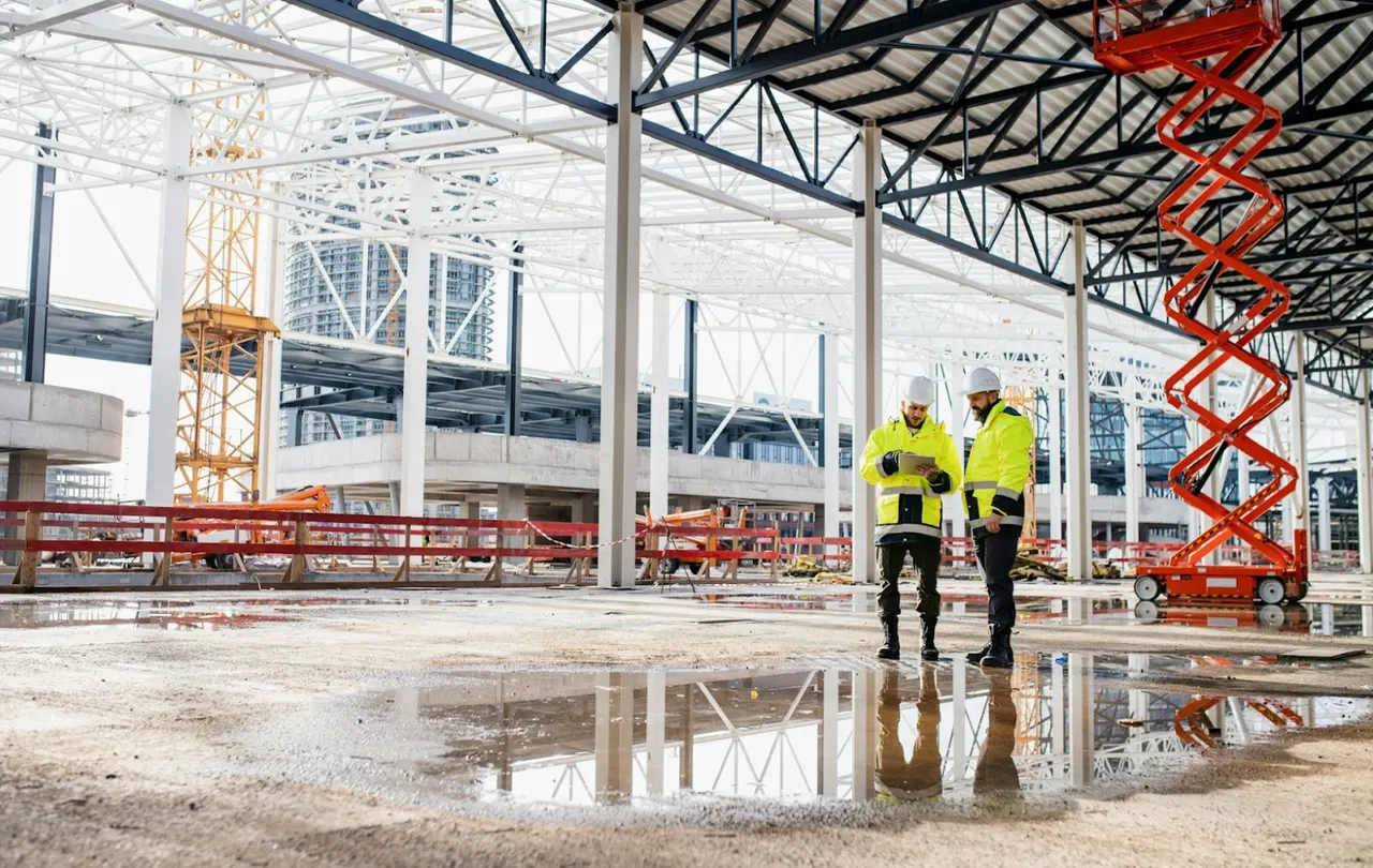 Engineers reviewing plans at a commercial outdoor construction site with standing water, illustrating real-world moisture exposure conditions that require water resistant wire and cable with UV-rated jackets and wet-location performance.