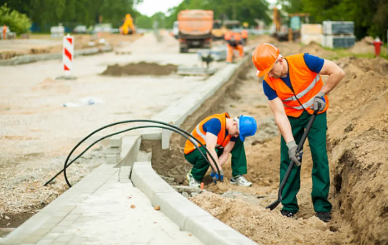 Workers installing underground cable in a trench for direct burial in commercial construction environment.